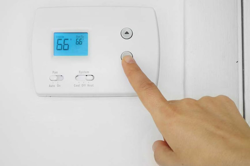 5 Reasons Why Regular HVAC Maintenance is Essential for Maricopa County Homeowners. Image is a photograph of a person's hand adjusting a wall mounted thermostat temperature.